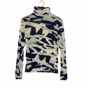 May include: A white long-sleeved turtleneck shirt with a black geometric pattern.