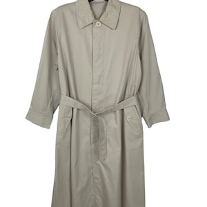 Puede incluir: Una gabardina beige con cinturón y dos bolsillos. La gabardina tiene cierre de botón y cuello.