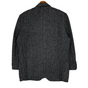 Puede incluir: Un blazer gris y negro con estampado de espiga, solapa con muescas y dos bolsillos delanteros. La chaqueta est&aacute; hecha de una tela texturizada y tiene un corte cl&aacute;sico y entallado. El blazer est&aacute; colgado de una percha de madera.
