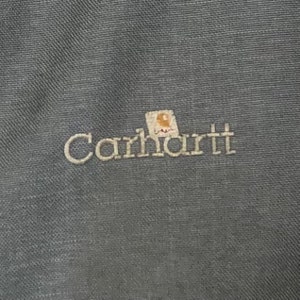 May include: A dark gray Carhartt workwear jacket with the Carhartt logo embroidered on the front.