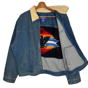 Pode incluir: Casaco de ganga azul com gola de veludo cotel&ecirc;. O casaco apresenta um forro estampado colorido com um desenho de &aacute;guia. Possui fecho de correr e dois bolsos frontais.