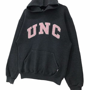 May include: A dark gray hooded sweatshirt with a pink UNC logo on the front. The sweatshirt has a kangaroo pocket and a drawstring hood.