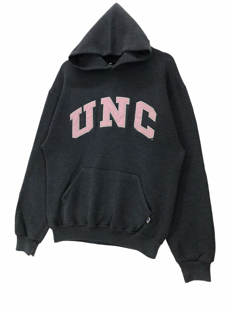 May include: A dark gray hooded sweatshirt with a pink UNC logo on the front. The sweatshirt has a kangaroo pocket and a drawstring hood.