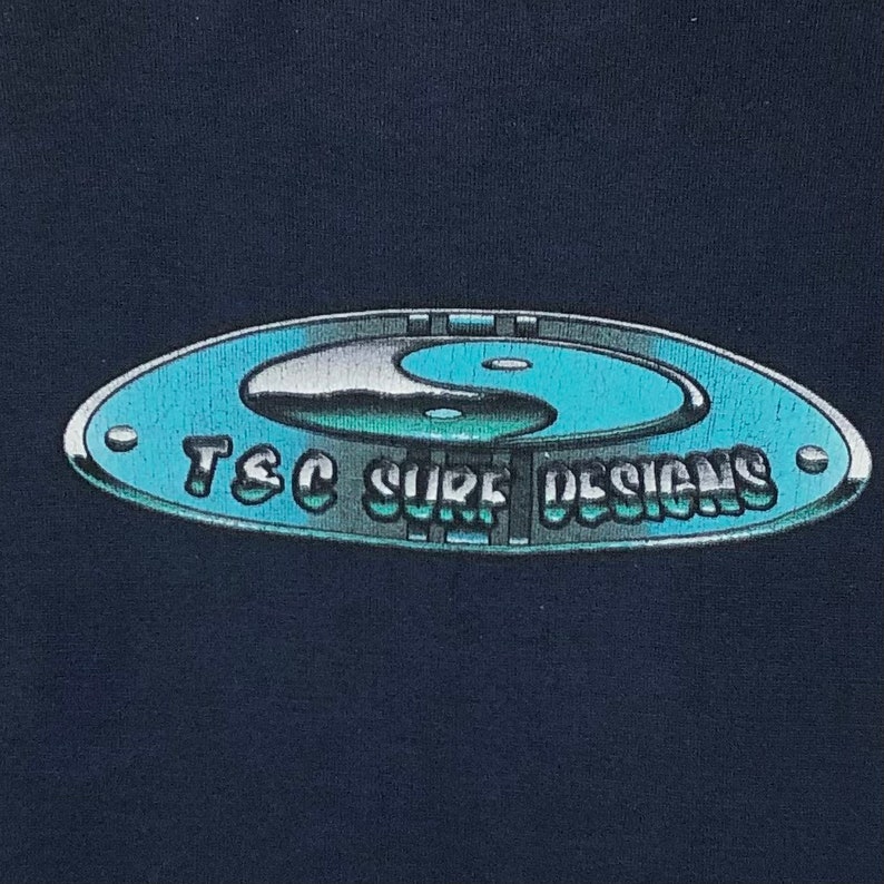 Pu&ograve; includere: Una maglietta nera con un simbolo yin yang argentato e blu all'interno di un cerchio argentato. Il testo "T&C Surf Designs" &egrave; scritto in un font argentato attorno al cerchio.