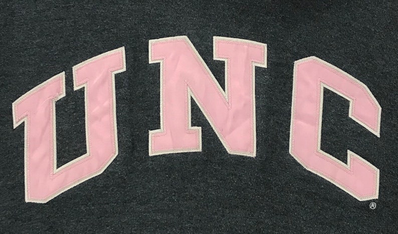 May include: Pink "UNC" lettering in a collegiate-style font on a dark gray background.