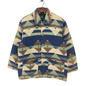 Puede incluir: Una chaqueta con estampado azul, marrón y beige con cierre de botones y dos bolsillos. La chaqueta tiene un diseño de estilo suroeste.