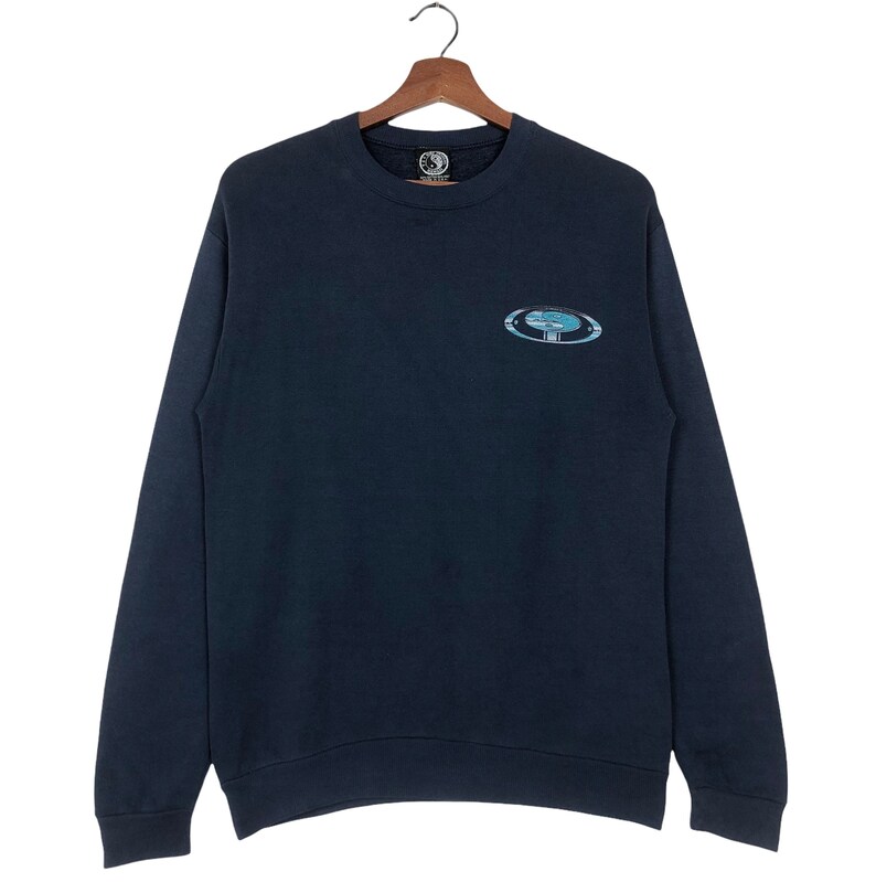 Pu&ograve; includere: Una felpa blu scuro con una grande grafica ovale sul davanti. La grafica &egrave; un design blu e bianco con la parola "Element" all'interno.