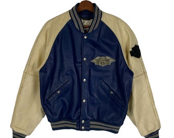 May include: A blue and cream leather varsity jacket with a Harley Davidson logo on the front. The jacket has a snap closure and a ribbed collar, cuffs, and hem.