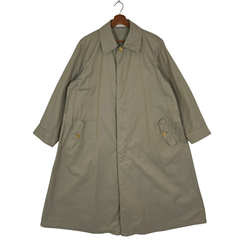 May include: A long, light brown trench coat with a button closure and two flap pockets. The coat has a classic design and is made of a durable fabric.