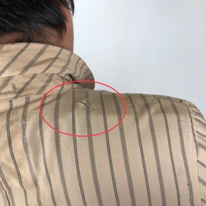 K&ouml;nnte beinhalten: Ein beige gestreiftes Hemd mit einem kleinen Loch in der Schulterpartie.