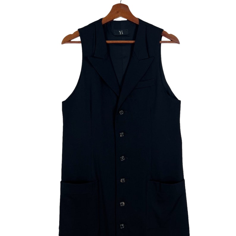 May include: A long black sleeveless vest with a button-up front and two pockets. The vest has a Y-3 label on the inside.
