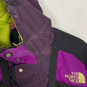 May include: Purple and black jacket with a green hood and the logo "THE NORTH FACE" on the right side.