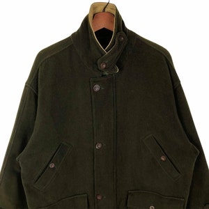 Pu&ograve; includere: Un cappotto di lana verde scuro con collo alto e chiusura con bottoni. Il cappotto ha due tasche anteriori e una fodera marrone chiaro visibile sul colletto. Uno stile classico, adatto al clima freddo.