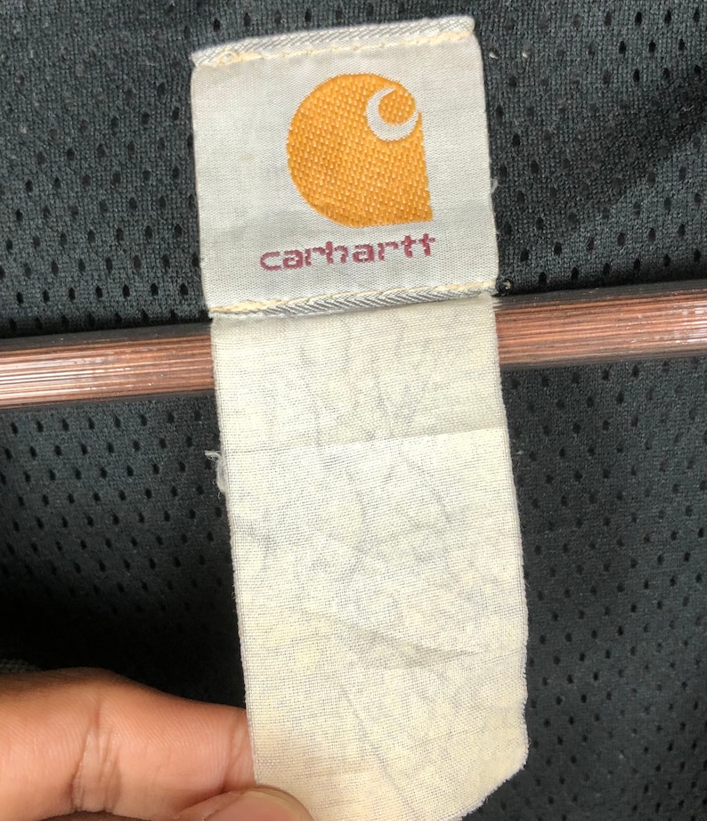 May include: A white Carhartt brand label with a yellow logo and the word "carhartt" in black lettering.