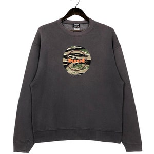 May include: A dark gray sweatshirt with a large, circular logo featuring a camouflage pattern and the word "FUCT" in orange letters.