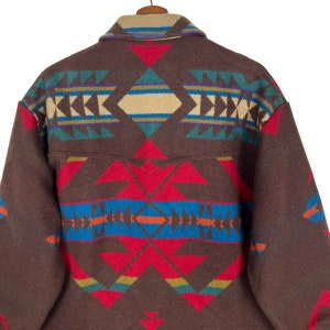 May include: A brown wool jacket with a colorful geometric pattern on the back. The pattern includes red, blue, green, and tan shapes. The jacket has a collar and a pocket detail.