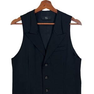 May include: A black sleeveless waistcoat with a pointed collar and five buttons. The waistcoat has a label that reads "Y's".