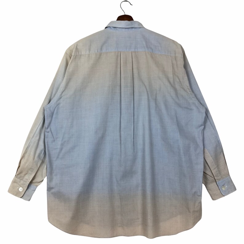 Op de afbeelding: Een lichtblauw overhemd met lange mouwen en knopen, met een vervaagd ombre-effect, dat overgaat van donkerblauw naar een lichter beige.