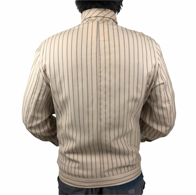 K&ouml;nnte beinhalten: Eine beige gestreifte Jacke mit Rei&szlig;verschluss. Die Jacke hat einen Stehkragen und lange &Auml;rmel.