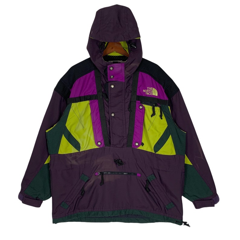 May include: A purple, green, and black The North Face ski jacket with a hood. The jacket has a zipper closure and multiple pockets.