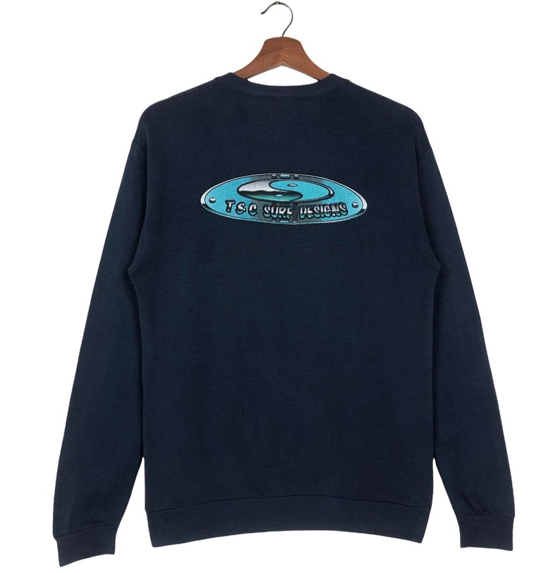 Pu&ograve; includere: Una felpa blu navy con una grafica bianca e blu di un simbolo yin yang e il testo "TSC Surf Designs".