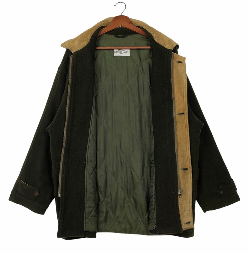 Pu&ograve; includere: Cappotto Longchamp verde scuro con colletto e finiture in pelle scamosciata beige. Il cappotto ha una fodera trapuntata verde oliva e una cerniera a tutta lunghezza. Il cappotto presenta anche due tasche con bottoni e una chiusura con bottoni.