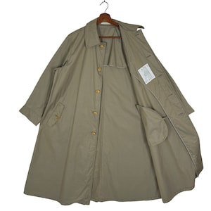 May include: A long, beige, cotton trench coat with a button closure and a single pocket on the left side. The coat is unlined and has a label on the inside that reads "Impeccably Made in Italy".