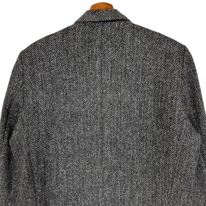Puede incluir: Primer plano de una blazer de tweed gris y negro con dise&ntilde;o de espiga. La chaqueta presenta solapas con muescas y un dise&ntilde;o cl&aacute;sico y entallado. La tela tiene una textura sutil y una paleta de colores neutros, adecuada para diversas ocasiones.