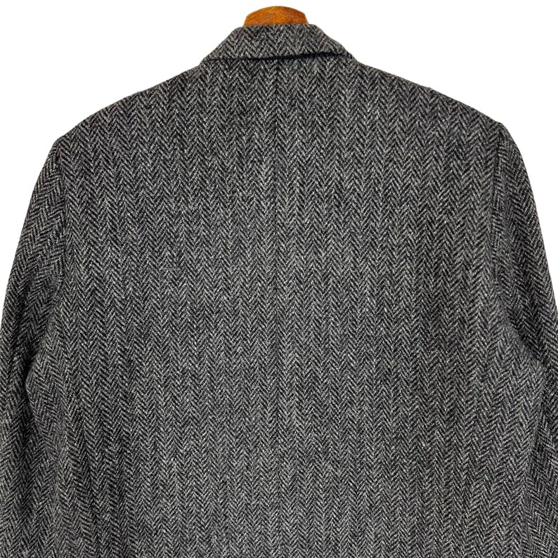 Puede incluir: Primer plano de una blazer de tweed gris y negro con dise&ntilde;o de espiga. La chaqueta presenta solapas con muescas y un dise&ntilde;o cl&aacute;sico y entallado. La tela tiene una textura sutil y una paleta de colores neutros, adecuada para diversas ocasiones.