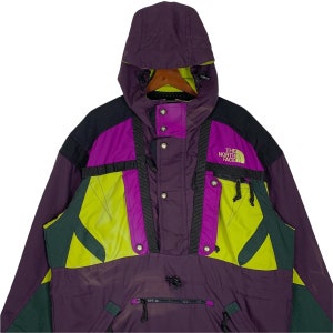 May include: A purple, green, and black ski jacket with a hood. The jacket has a zipper closure and multiple pockets. The North Face logo is on the front of the jacket.