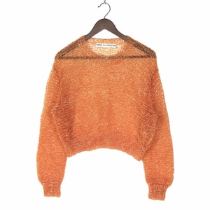 May include: A loose-fitting, orange, sparkly, knit sweater with long sleeves. The sweater has a round neckline and is cropped. The label "COMME des GARCONS" is visible on the front of the sweater.
