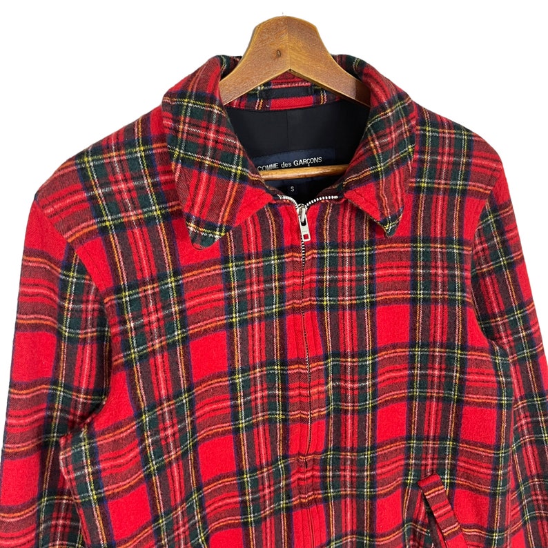 May include: Red, green, and yellow plaid jacket with a zipper closure. The jacket has a black label with the text "COMME des GARCONS" on the collar.