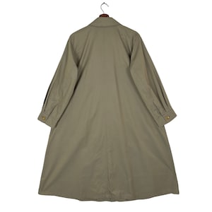 May include: A long, light brown, collared, button-up coat with long sleeves and a single button at the cuff. The coat has a center seam down the back and a single button at the neck.