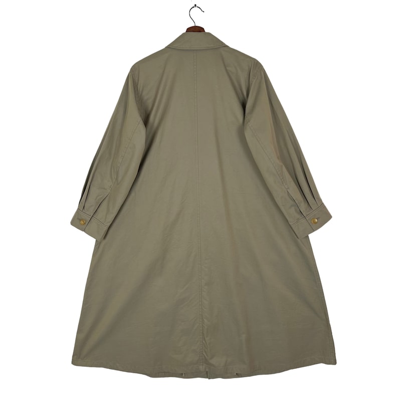May include: A long, light brown, collared, button-up coat with long sleeves and a single button at the cuff. The coat has a center seam down the back and a single button at the neck.