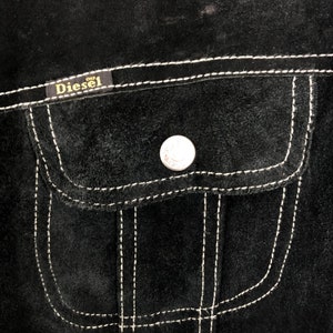 Puede incluir: Chaqueta de ante negro con un bolsillo cosido blanco y un parche con el logotipo de Diesel.