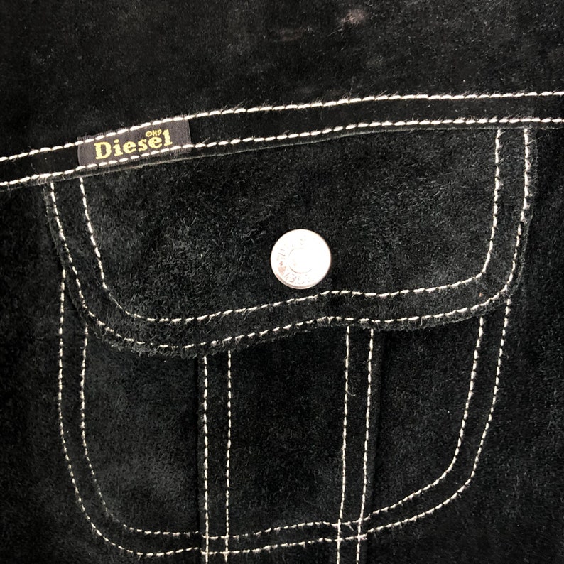 Puede incluir: Chaqueta de ante negro con un bolsillo cosido blanco y un parche con el logotipo de Diesel.