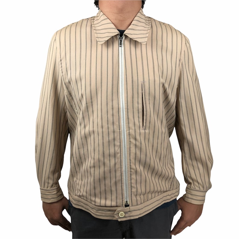 K&ouml;nnte beinhalten: Eine beige gestreifte Jacke mit Rei&szlig;verschluss und einer kleinen Tasche auf der linken Seite.