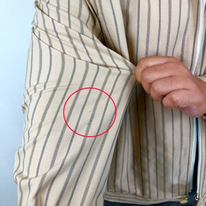 K&ouml;nnte beinhalten: Ein beige gestreiftes Hemd mit einem kleinen braunen Fleck auf dem &Auml;rmel.