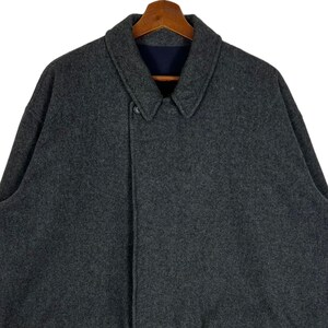 May include: A dark gray wool coat with a single button closure and a collar. The coat is hanging on a wooden hanger.
