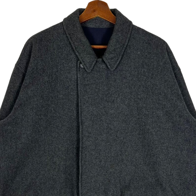 May include: A dark gray wool coat with a single button closure and a collar. The coat is hanging on a wooden hanger.