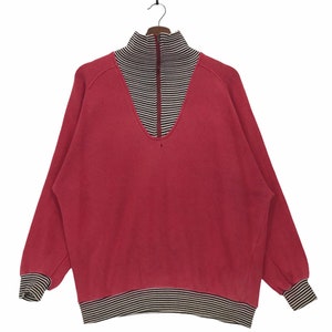May include: A red, long-sleeved sweater with a black and white striped collar and cuffs. The sweater has a half-zip closure.