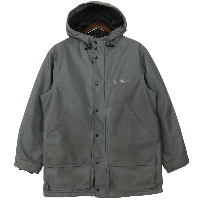 May include: A gray Carhartt hooded jacket with a button front closure and two large pockets on the front. The jacket has a logo on the left chest that says "Carhartt".