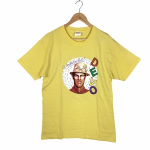 Op de afbeelding: Geel T-shirt met korte mouwen met een grafische print van een man met een hoed en de tekst "Are We Not Men?" en "DEVO" in kleurrijke letters.