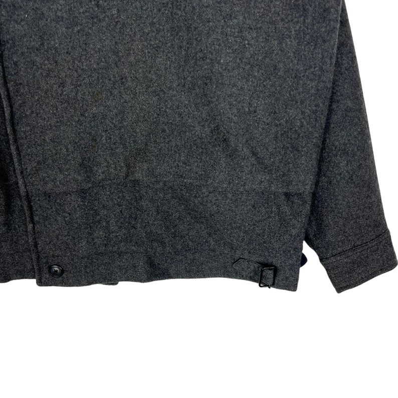 May include: A dark gray wool jacket with a button closure and a strap on the bottom.