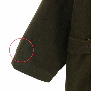 Pu&ograve; includere: Primo piano di una manica di cappotto verde oliva scuro. La manica &egrave; realizzata in un materiale spesso, forse lana. Il cappotto ha un design classico con una vestibilit&agrave; sartoriale. L'immagine evidenzia la trama e il colore del tessuto.
