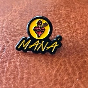 May include: Black and yellow enamel pin with a stylized heart and the word "MANA" in a black and yellow font.