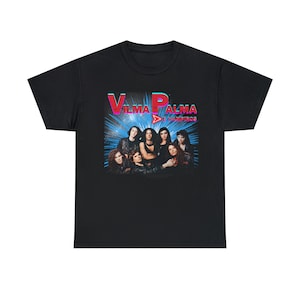 Puede incluir: Camiseta negra con un gráfico de una banda llamada "Vilma Palma e Vampiros". Los miembros de la banda aparecen en una foto de grupo con un fondo azul y blanco.