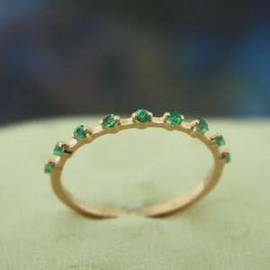 Pode incluir: Um anel de banda de ouro com uma fileira de pedras preciosas verde esmeralda.