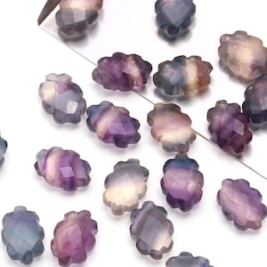 May include: A collection of 20 purple, blue, and white fluorite gemstone beads in a faceted oval shape. The beads have a unique, wavy, and textured surface.