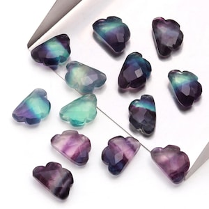 Może przedstawiać: Kolekcja 12 iryzujących fioletowych, zielonych i niebieskich koralików z fluorytu w kształcie chmury. Koraliki są rozrzucone na srebrnej tacy.